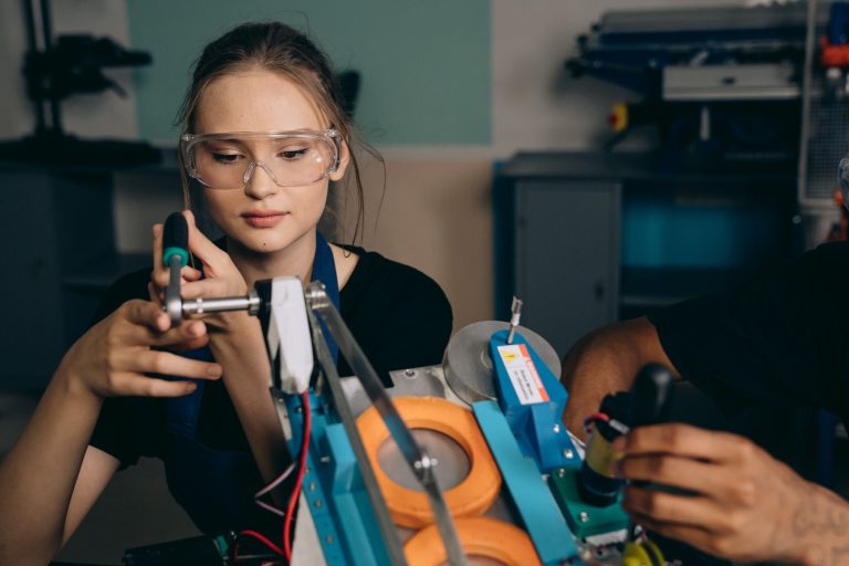 A student in safety glasses assembling a robotic device in a workshop