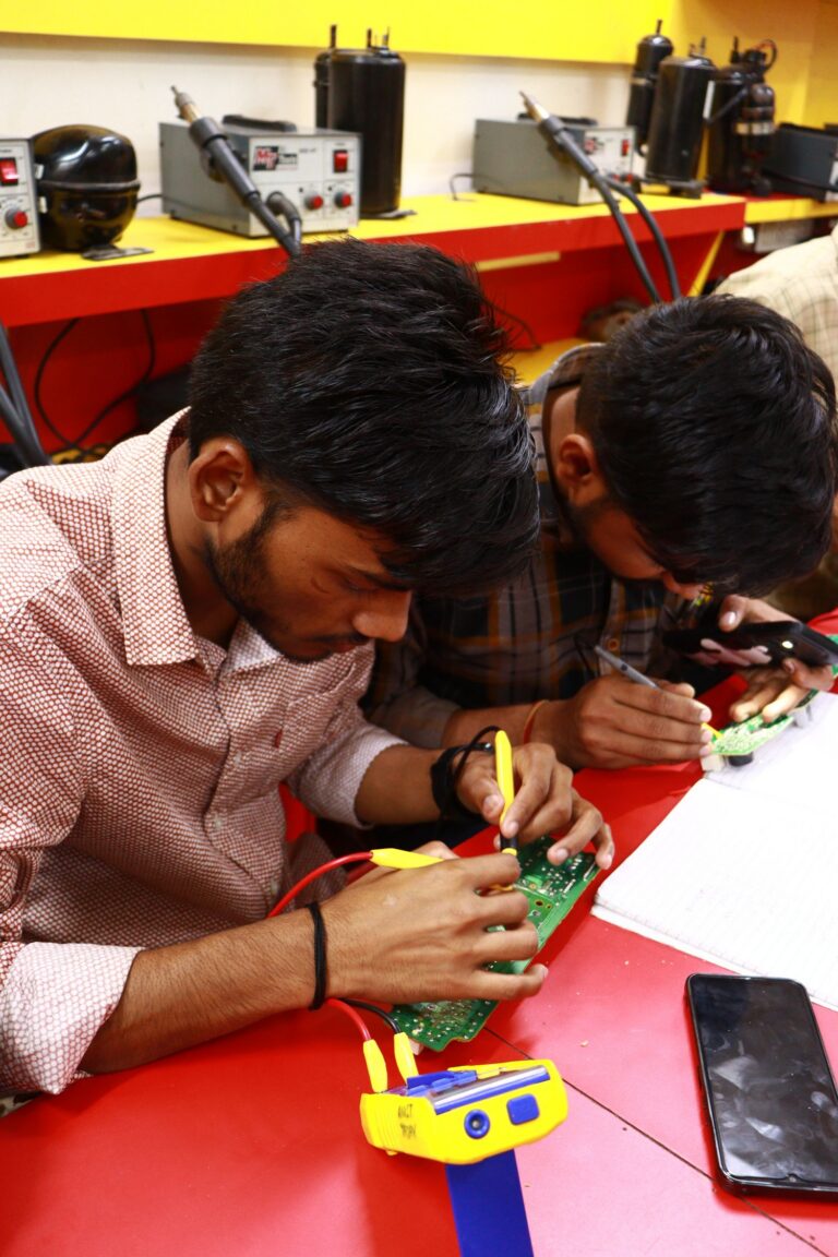 Two students soldering a circuit board in an electronics lab